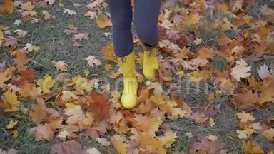 女人穿着靴子踏上秋天的公园，踢黄落叶